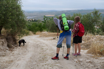 Two Backpackers Hiking on a Rural Path Accompanied by a Dog