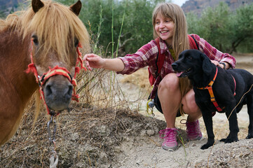 Woman and Black Dog Engaging with a Miniature Horse in a Scenic Outdoor Setting