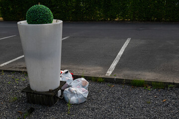 A few trash bags left in plastic bags next to a concrete planter.
