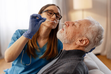Nurse performing nasal swab test on senior man at home selective focus, closeup