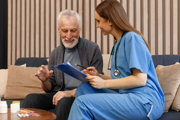 Smiling nurse explaining treatment to senior man on sofa at home