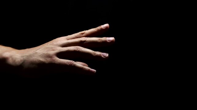 A man's hand reaching towards the light.
Religion theme.
Human hand on a dark background.
A symbol of hope, help and kindness in hopeless situations.