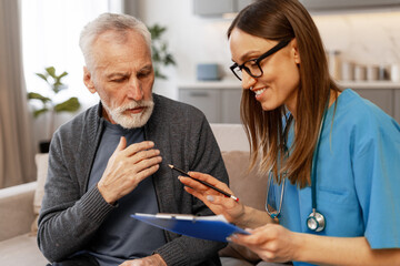 Female doctor visiting elderly man at home taking notes on clipboard