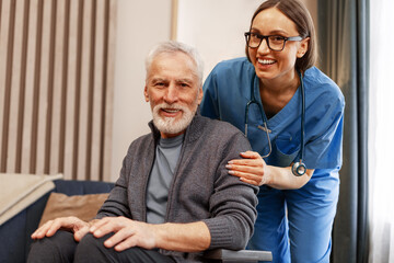 Caring nurse assisting elderly man in wheelchair hugging looking at camera
