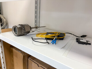 Industrial sensor and fiber optic cables placed on a white shelf in a technical storage room.