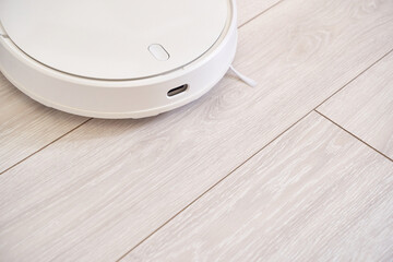 Modern white robotic vacuum on light wood floor in minimalist home setting for efficient cleaning.