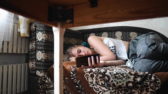 A woman lies with a sad look on the sofa in the kitchen and looks at the phone.