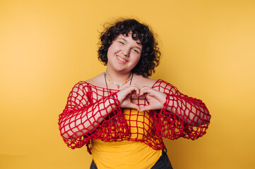 Smiling young woman creates a heart shape with her hands against a bright yellow background
