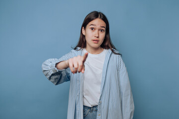 Young woman gestures with finger pointing against a blue background during casual indoor setting