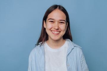 Young woman smiles brightly against a light blue background in a casual outfit, radiating happiness...