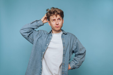 Young man with tousled hair poses thoughtfully against a solid blue background in a casual outfit