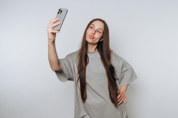 Young woman takes a selfie in casual outfit against a neutral background while posing playfully