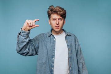 Man showing a small size gesture against a blue background during a casual indoor setting