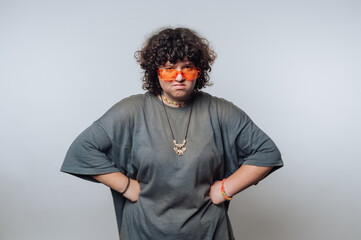 Person with curly hair wearing sunglasses stands in studio with hands on hips, showcasing a...
