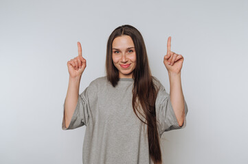 Young woman with long hair smiling and pointing upwards in a bright, minimalistic space