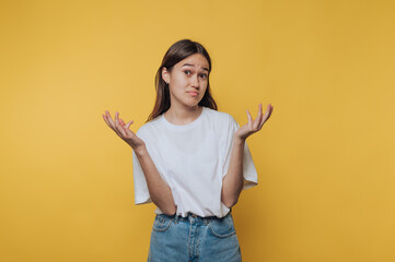 Confused young woman gestures with hands against a bright yellow background