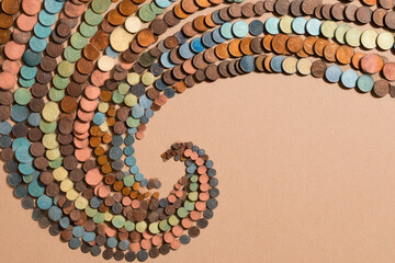 Spiral of assorted coins in various colors and sizes arranged on soft beige background, creating dynamic wave pattern with blank circle at center, evoking creativity and movement