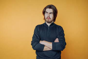 Young man expressing annoyance with crossed arms and serious facial expression in a vibrant orange background