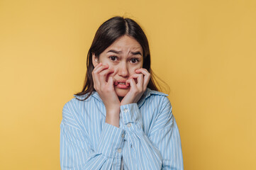 Young woman expresses anxiety against a bright yellow background while wearing a light blue shirt