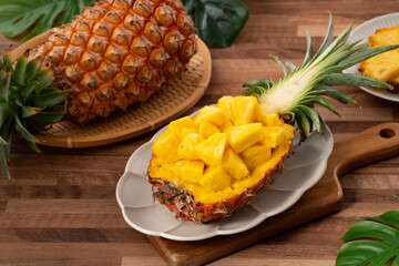 Fresh pineapple chunks served in a pineapple bowl on wooden table background.
