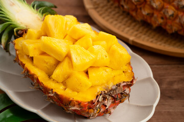 Fresh pineapple chunks served in a pineapple bowl on wooden table background.