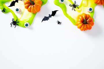 Halloween flat lay composition with pumpkins, black spiders, bats, fake eyeballs, and dripping green slime on white background