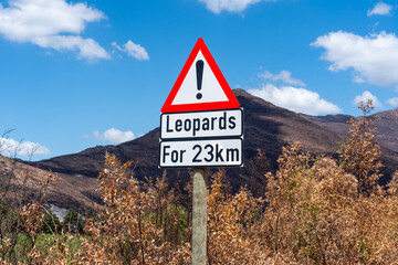 Verkehrsschild warnt vor Leoparden auf 23 Kilometern, vor bergiger, trockener Landschaft