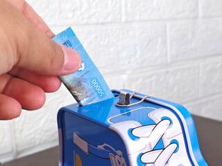 Saving Indonesian Rupiah Hand Putting Money in Sneaker Piggy Bank.