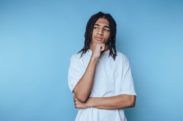 Young person in white shirt thinking with hand on chin against blue background