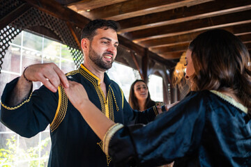 Multiethnic couple smile and dance during Arab celebration with friends and family, dressed in...