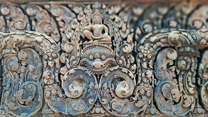 Intricately carved sandstone relief from Banteay Srei temple in Siem Reap province, Cambodia, depicting a guardian figure and Hindu deity in detailed floral and mythological patterns.