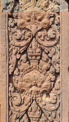 Close-up of sandstone carving at Banteay Srei temple in Siem Reap, Cambodia, showing mythological guardian face and floral ornament in classic Khmer style.