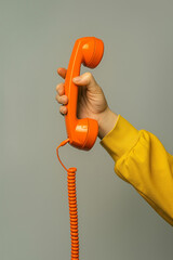 Person holding orange telephone receiver in hand. Vintage communication and retro tech theme.
