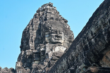Giant stone face carved into the Bayon temple tower under clear blue sky in Angkor Thom, Cambodia.