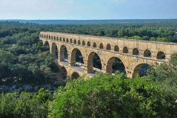 Obraz premium Ancient Roman aqueduct Pont du Gard crossing a lush green valley in southern France, viewed from above