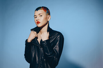 woman with colorful hair and leather jacket posing confidently against blue background, bold...