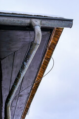 Close-up of an old metal rain gutter and snowy roof edge with visible wooden eaves and wires...