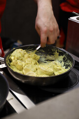 chef cocinero cocinando tortellini en una sartén en la vitrocerámica de la cocina