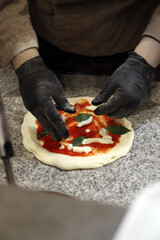 chef experto en pizza elaborando con sus manos con guantes una pizza artesanal en la masa base y sus ingredientes 