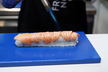 chef experto en sushi flambeando salmón ahumado fresco en un rollo con arroz