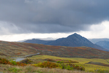 A winding road leads through a vast, colorful Altai mountain landscape under dramatic storm clouds,...