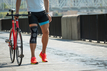 Cyclist walks with bandage on knee at public park. Unhappy cyclist with knee pain and injury...