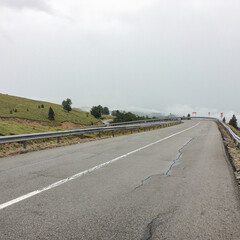 Fototapeta premium Mountain road near Novaci, Gorj County, Romania, on a cloudy and rainy day with a view of wet asphalt and scenic curves.
