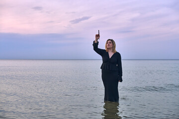 Young woman stands waist-deep in ocean during sunset, holding paintbrush. Serene seascape evokes...