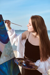 Young female artist creates portrait on canvas with serene beach backdrop. Tranquil environment...