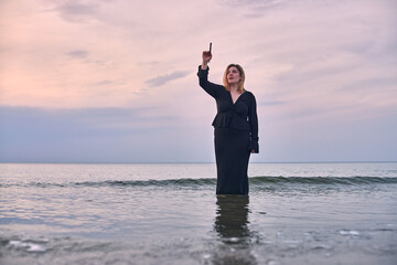 Young woman stands waist-deep in ocean during sunset, holding paintbrush. Serene seascape evokes...