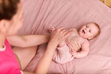 Young caucasian mother with brown hair engages infant in passive leg exercises. Soft lighting on...