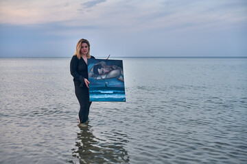 Young woman stands in calm ocean waters, holding surreal painting. Scene evokes tranquility and...