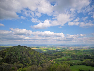 Obraz premium Panoramic spring view over the Moravian countryside with forested hill and the Chapel of Saint Barbara, under a sky full of dramatic clouds and blue patches.