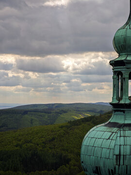 Close-up of the green copper dome and tower of Buchlov Castle with lush green hills in the background under a dramatic cloudy sky. South Moravia, Czech Republic.